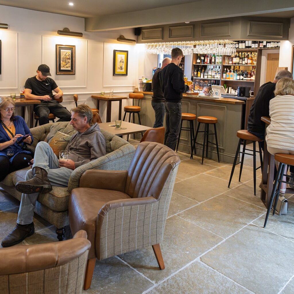 The bar and lounge at The Fox at Walton, Wetherby — guests on tub chairs and bar stools with the drinks bar in the background